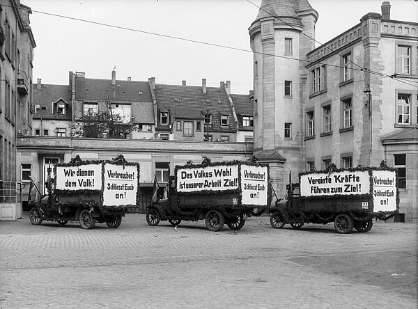 Mit Werbetransparenten ausgestattete LKWs im Hof des Lebensbedürfnisvereins um 1925
