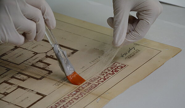 Ein wichtige Kernaufgabe des Stadtarchivs ist die dauerhafte Erhaltung seiner Archivalien, die mitunter umfangreiche Konservierungs- und Restaurierungsmaßnahmen erfordert. Zum Verschließen eines Risses im Plan wird hier Japanpapier mit Kleister aufgebracht. 