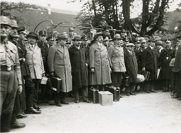 Ankunft der Sozialdemokarten im KZ Kislau, vermutlich gestellte Aufnahme der Schutzhäftlinge von SS-und SA-Leuten umringt; von links nach rechts: Hermann Stenz, Adam Remmele, Erwin Sammet, Ludwig Marum, Gustav Heller, Sally Grünebaum und August Furrer; Text auf der Rückseite des Fotos: "Die alte Spitze der Prominenten packen ihre Koffer, Karlsruhe 1933"