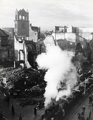 Fotografie der Trümmerbahn auf der Kaiserstraße im Jahr 1946. Links der zum Teil zerstörte Turm der Katholischen Stadtkirche St. Stephan.